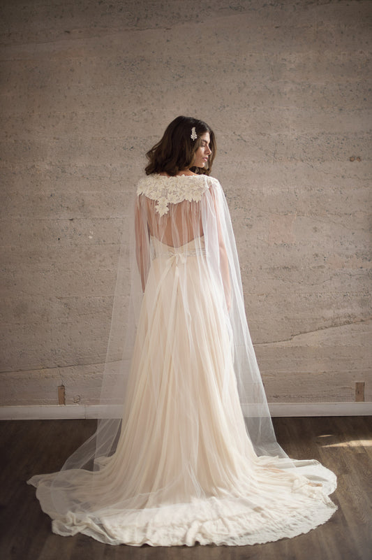 The DAENERYS Cape is the perfect statement bridal accessory for the bohemian bride. This bridal cape veil features a delicate hand embroidered floral pattern and pearl ivory beaded embellishments. Expertly crafted with a floor length sheer tulle this shoulder capelet adds a touch of elegance to any wedding dress. Wear it as an alternative to a traditional veil or to cover your shoulders during a ceremony.
